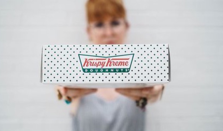 A screenshot of a woman holding a box of donuts from Krispy Kreme Doughnuts in Circus Circus Hotel and Casino Las Vegas.
