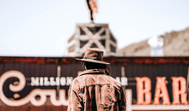 A screenshot of a man in western clothing standing outside of a country bar.